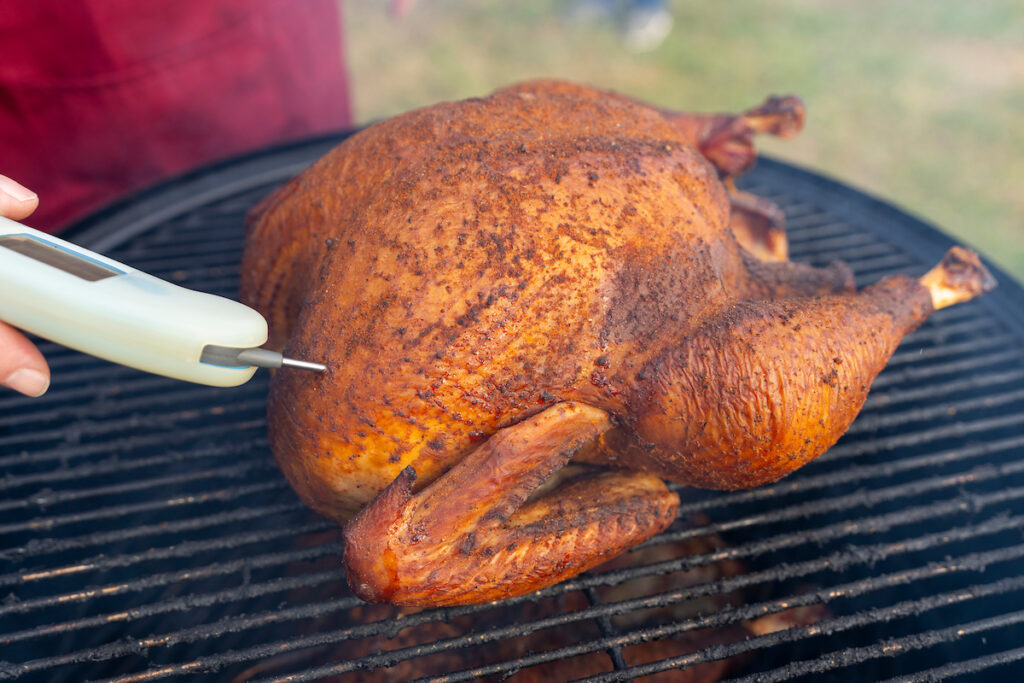 A roasted turkey sits atop a grill with a meat thermometer in it