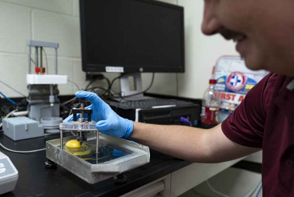 A man wearing blue gloves using a device to study an egg white.