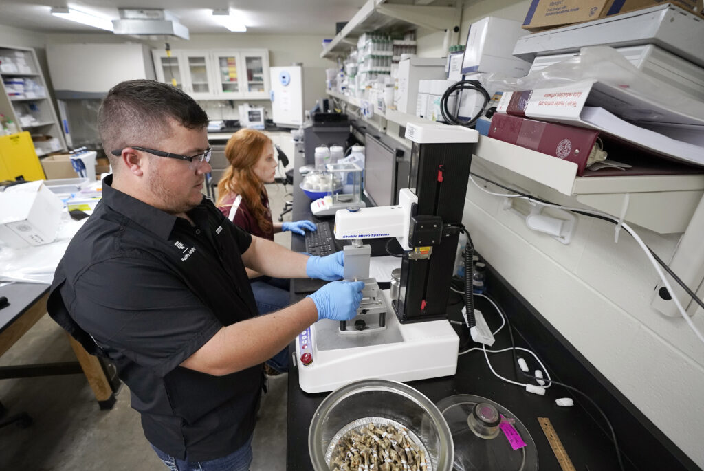A man in a lab coat examines a specimen under a microscope in a laboratory setting.