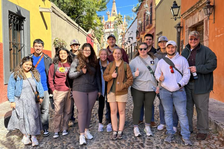 Study abroad students posing in front of colorful buildings on cobblestone street.